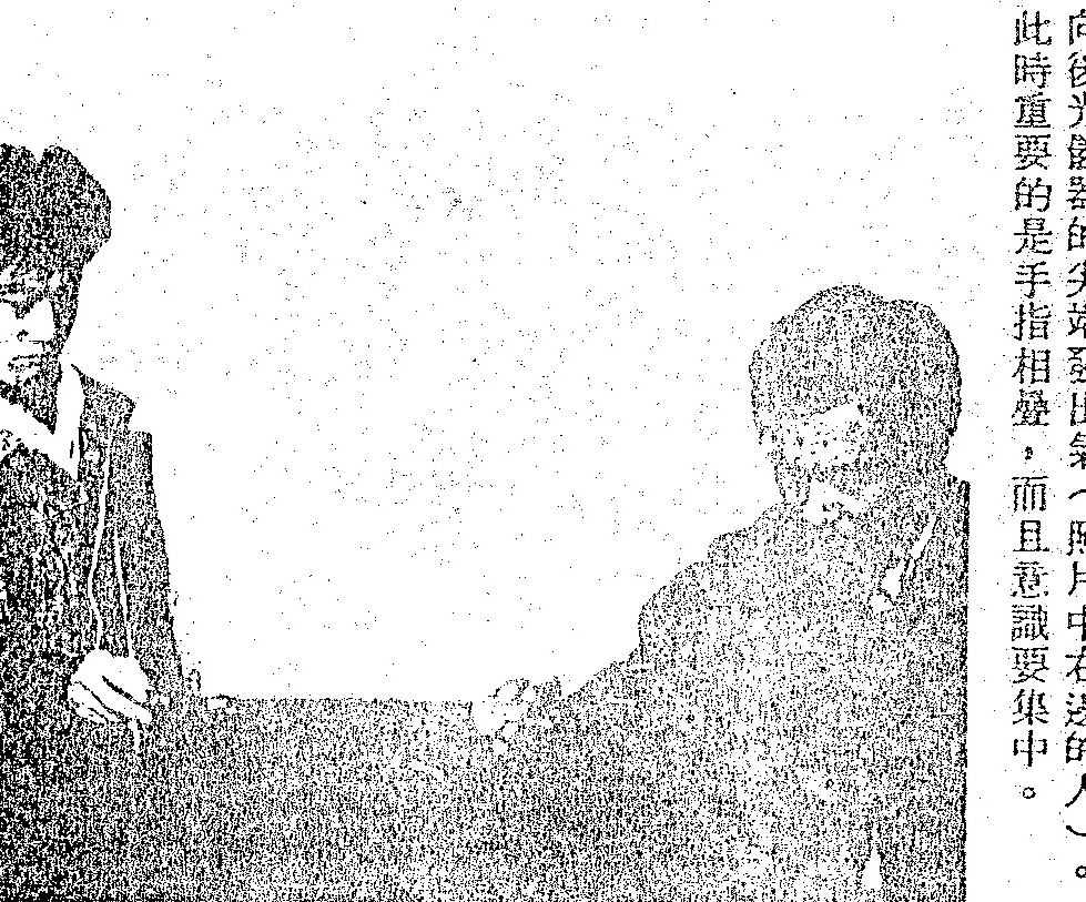 A grainy black-and-white photograph of two people. The person on the right is blowing air toward an instrument's tip. A vertical caption is printed directly within the image area on the right.