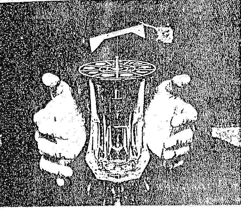 A black and white photograph showing two hands cupping a glass container topped with a mechanical rotor assembly, illustrating a demonstration of a rotary wing experiment.